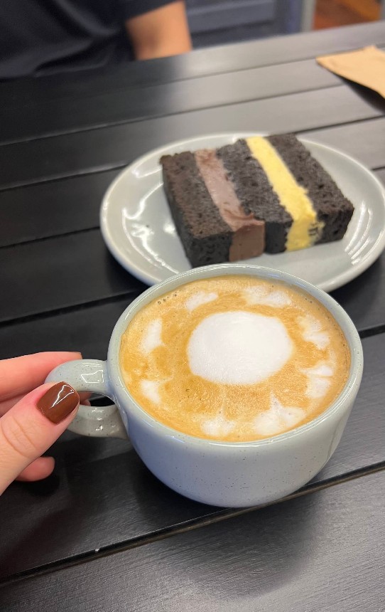 Cappuccino com latte art em xícara azul e torta de chocolate ao fundo