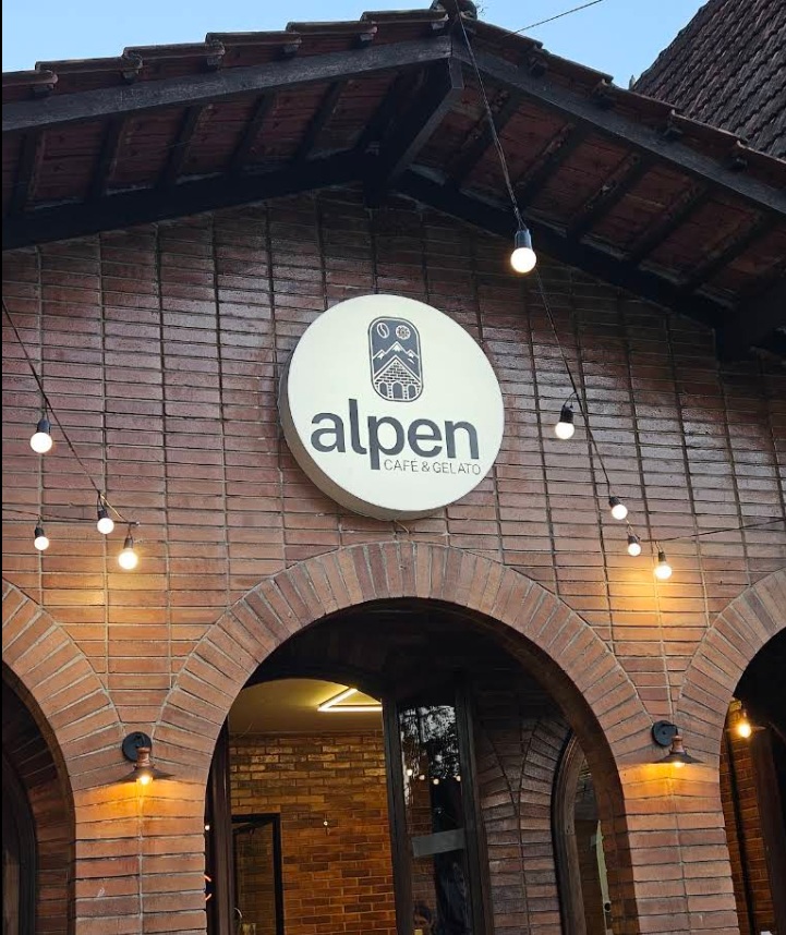 Fachada de tijolos da Alpen Café & Gelato com a placa da casa e luzes acesas